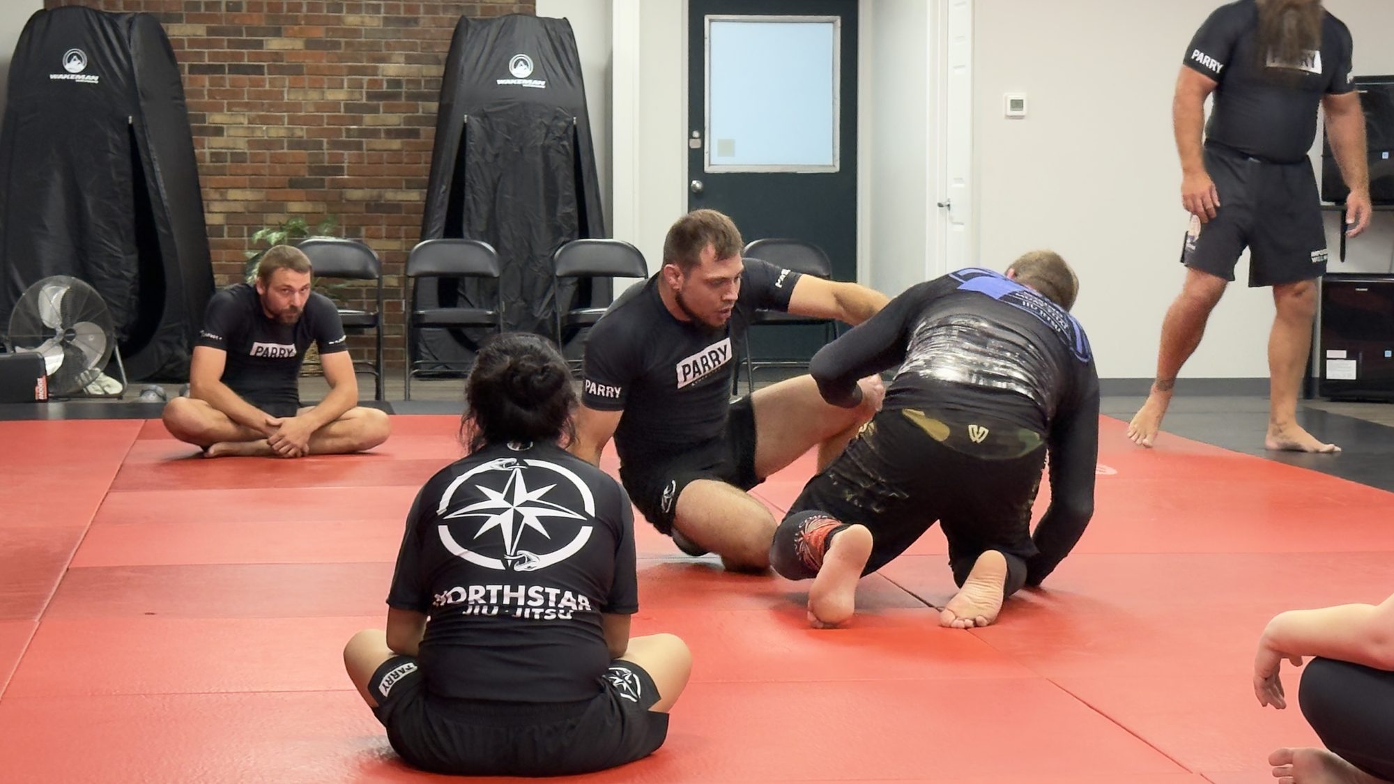 A Northstar Jiu Jitsu class in session in Eau Claire, with students watching from the mat while a pair drills a position