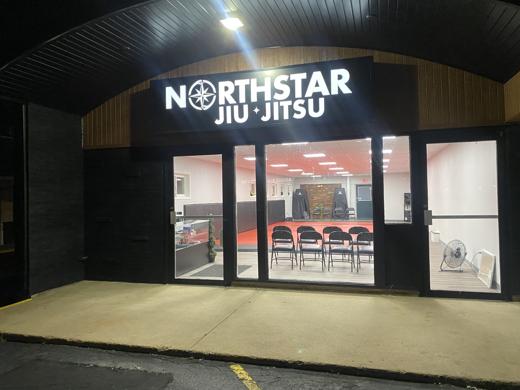 The lit Northstar Jiu Jitsu storefront sign and entrance at 2543 E Clairemont Ave in Eau Claire, Wisconsin, with the mat room visible through the front windows